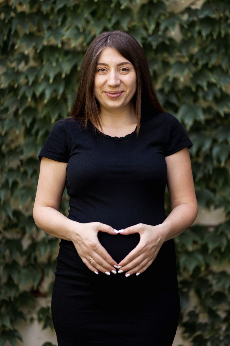 Pregnant woman in a black dress standing against a vibrant green wall.