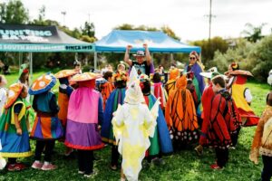 Children in vibrant costumes enjoy an outdoor event, smiling and playing together in a festive atmosphere.
