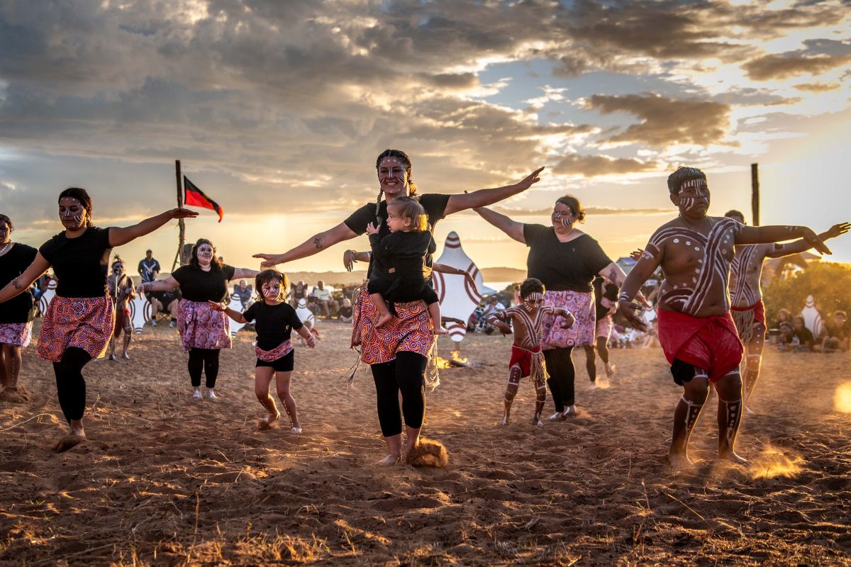 A group of people joyfully dancing on the sand during a vibrant sunset.