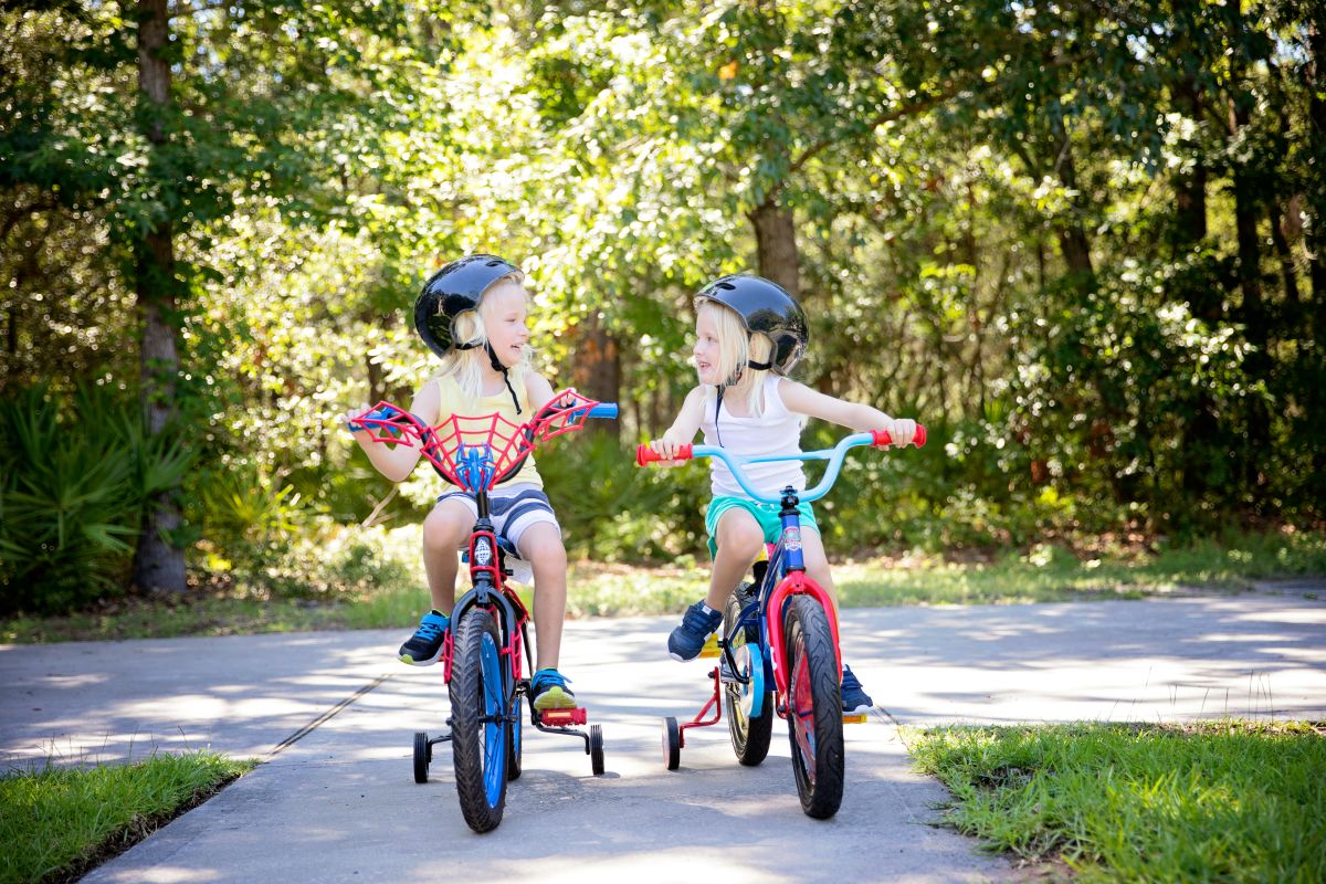  Two young children riding bikes side by side on a sunny paved path.