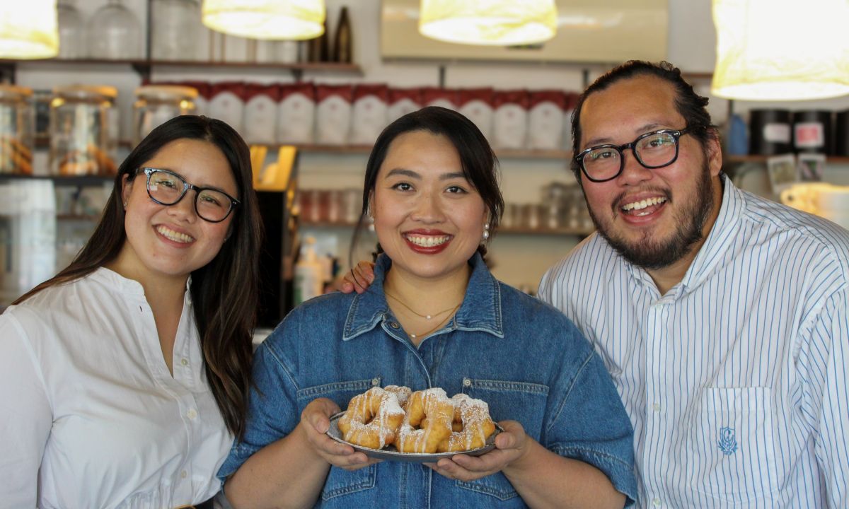 Three smiling people hold plates of food, enjoying a meal together in a cheerful setting.