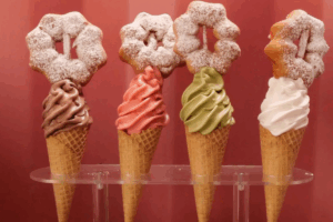 Four colourful ice cream cones topped with sprinkles, chocolate, fruit, and whipped cream.