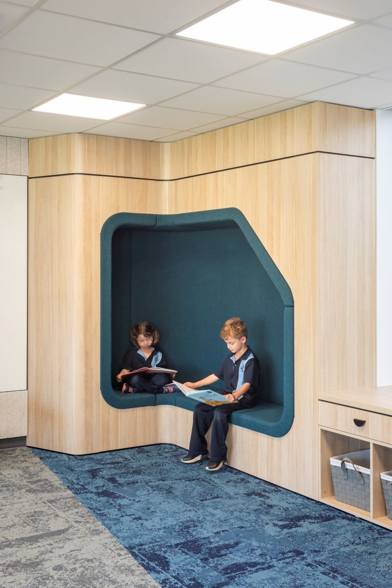 Two children sit together in a room with a bright blue wall behind them.