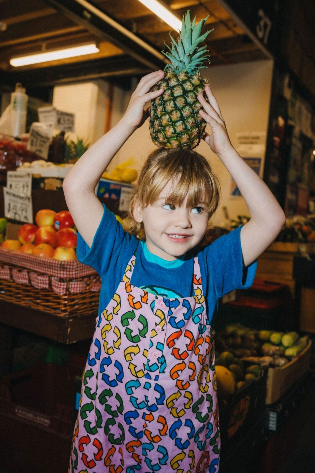 A child balances a pineapple on their head, smiling and enjoying a playful moment outdoors.