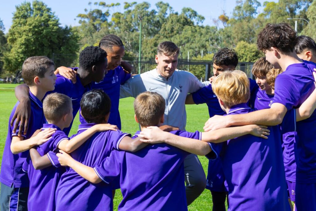A group of young boys in purple shirts huddle closely together, smiling and engaging with one another.
