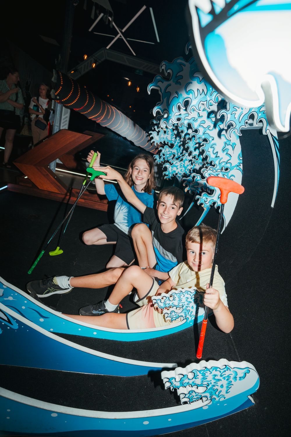 Three children joyfully play in a colorful water-themed room filled with aquatic decorations and playful water features. 