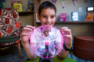 A young boy joyfully holds up a glowing pink light ball, smiling at the camera.