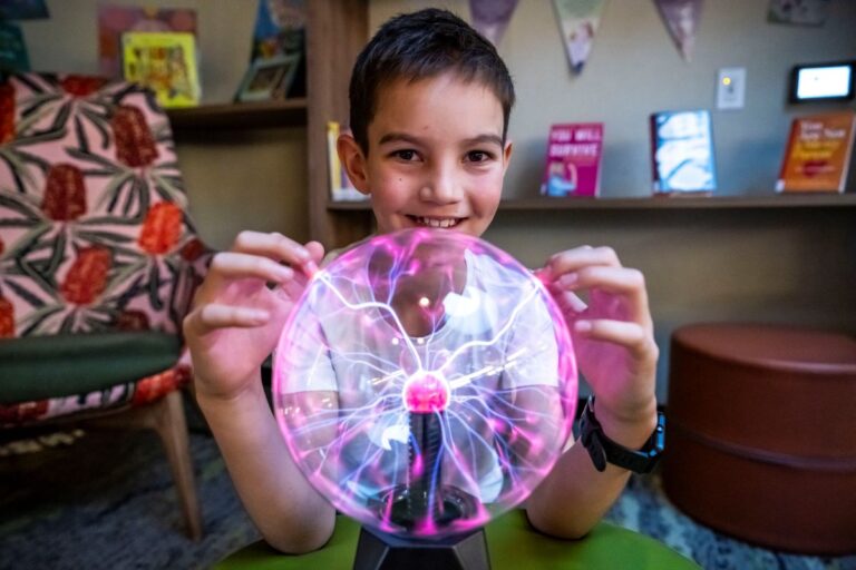 A young boy joyfully holds up a glowing pink light ball, smiling at the camera.