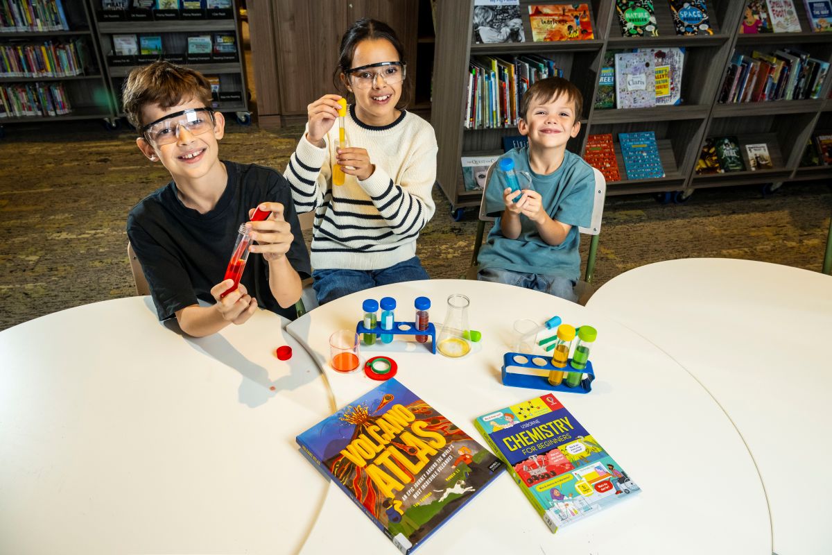 Three children engaged in a science experiment at a table, surrounded by colorful science kit materials.
