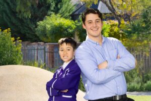 A man and a boy stand together in front of a school, smiling and enjoying their time outdoors.
