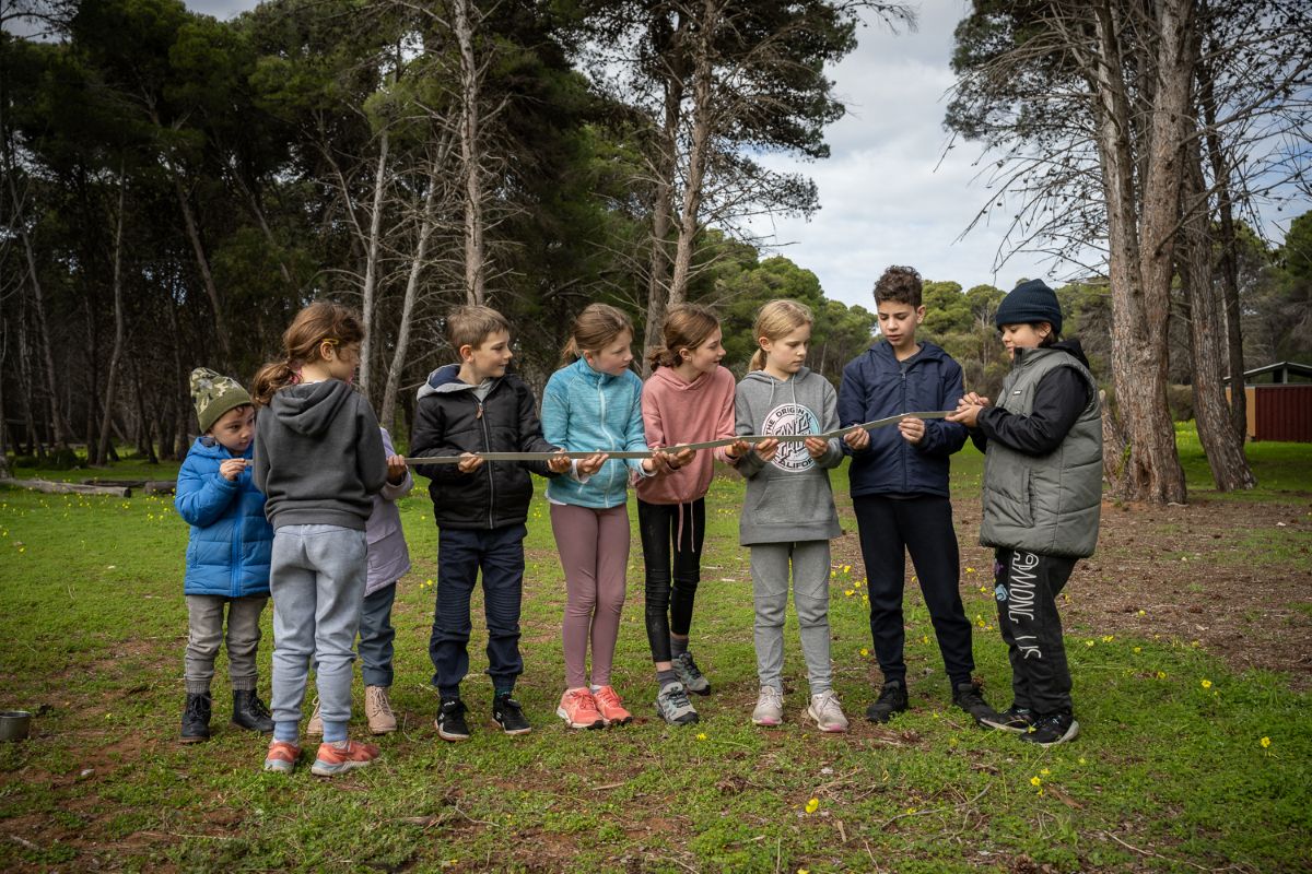 A group of children gathered around a large tree, smiling and interacting with each other in a playful setting.