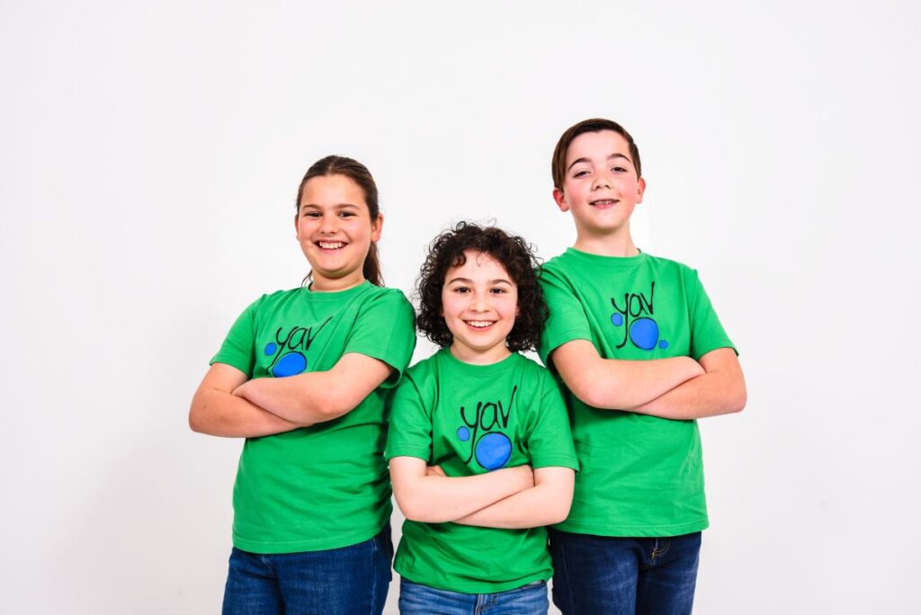 Three children in green shirts stand together, smiling and posing for the camera.