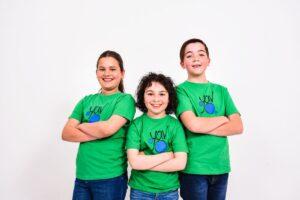 Three children in green shirts stand together, smiling and posing for the camera.