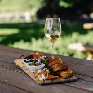 A wooden tray featuring an assortment of food and a glass of wine.