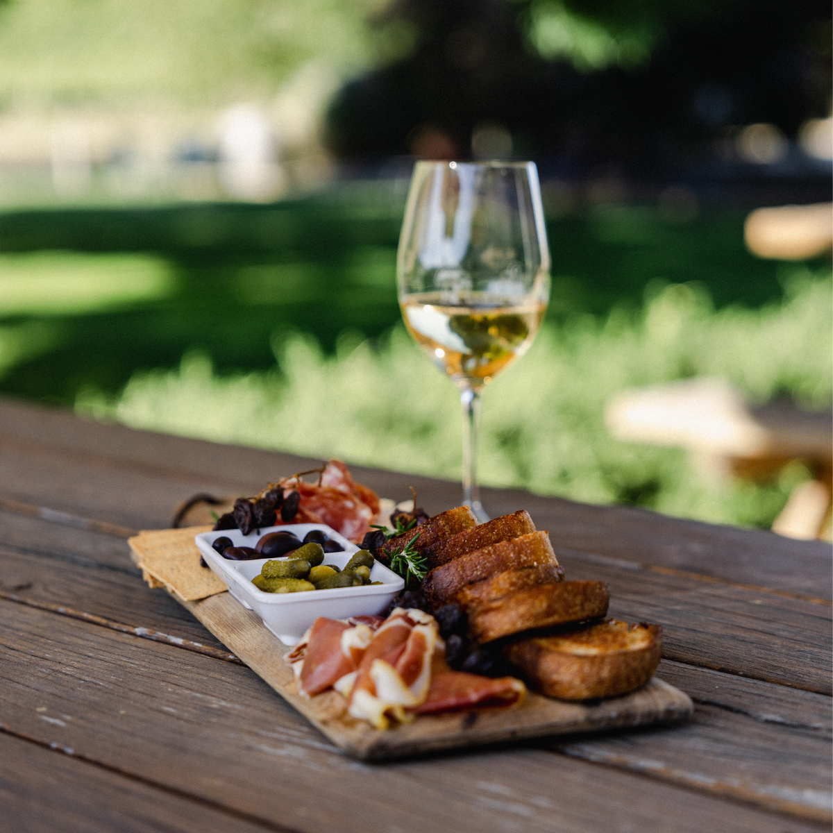 A wooden tray featuring an assortment of food and a glass of wine.