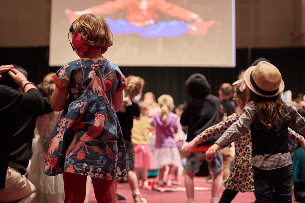 Children joyfully dancing in front of a large screen displaying colorful visuals.