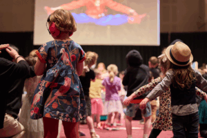 Children joyfully dancing in front of a large screen displaying colorful visuals.