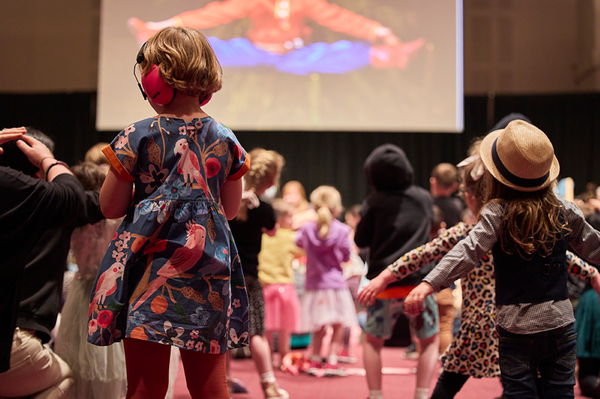 Children joyfully dancing in front of a large screen displaying colorful visuals.