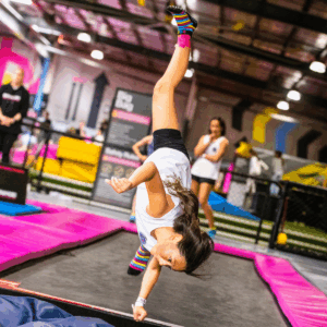 A young girl performs a handstand on a trampoline, showcasing her balance and agility in mid-air.