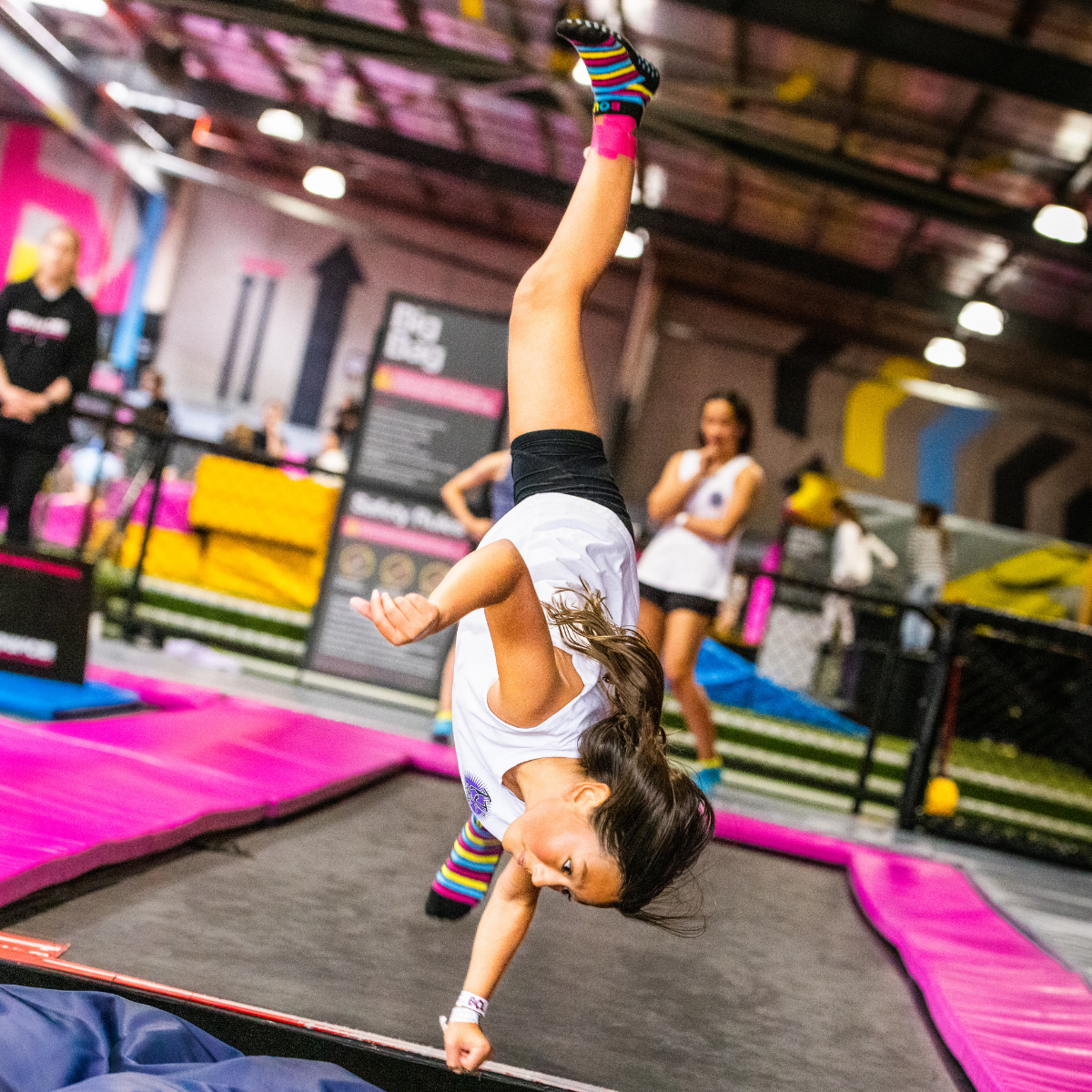 A young girl performs a handstand on a trampoline, showcasing her balance and agility in mid-air.