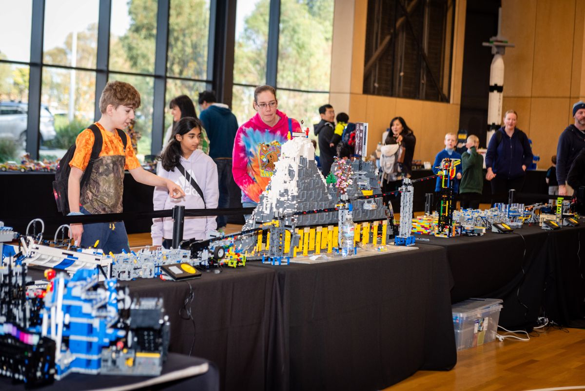 A group of people examines a table filled with colorful LEGO pieces, discussing their building ideas.