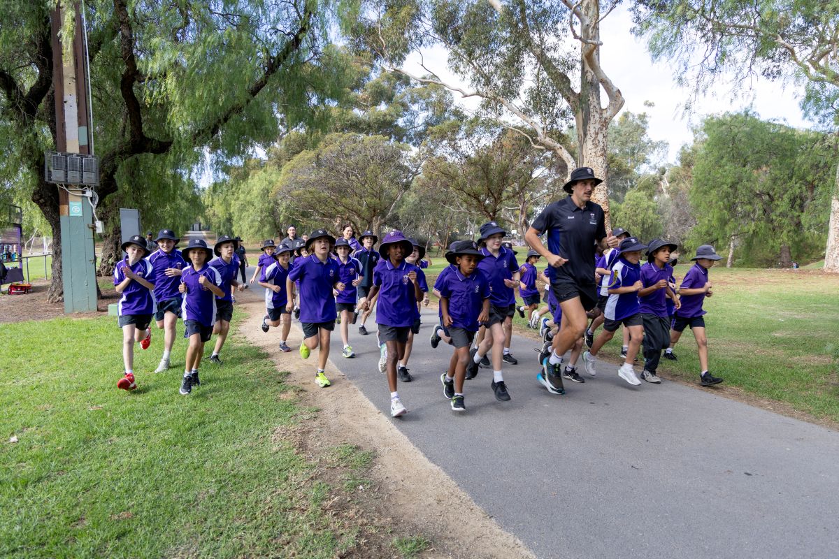 A group of school children walking together along a path surrounded by trees.