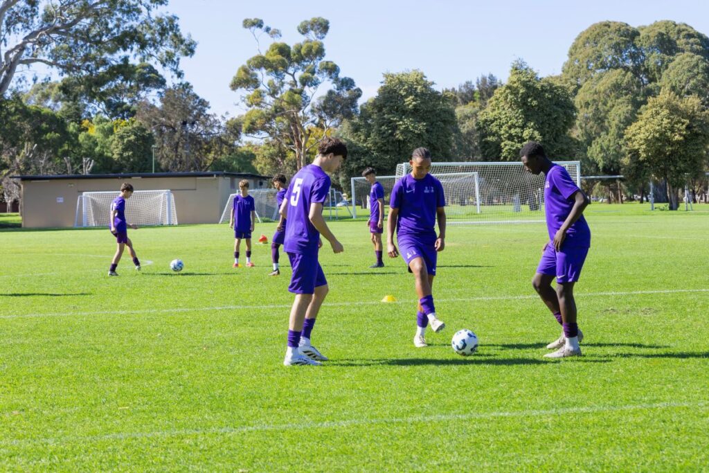 A group of young men playing soccer on a grassy field, focused on the ball and each other.