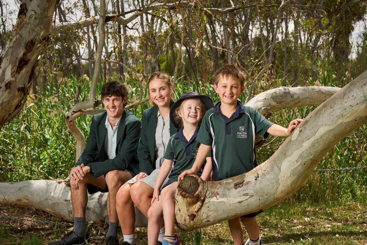 Faith Lutheran College students in uniforms sitting together on a tree branch, smiling and enjoying their time.