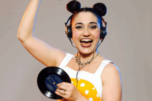 A woman in a polka dot dress smiles while holding a vinyl record in her hands.
