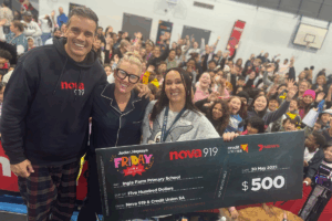 Two people and a dog smile while holding a large check, celebrating a financial achievement or donation.