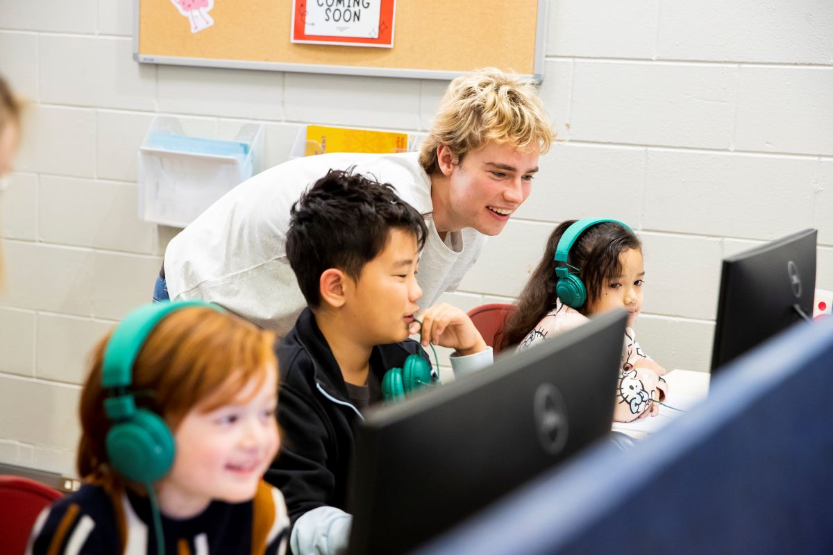 A teacher assists children with computers in a bright classroom, fostering a collaborative learning environment.