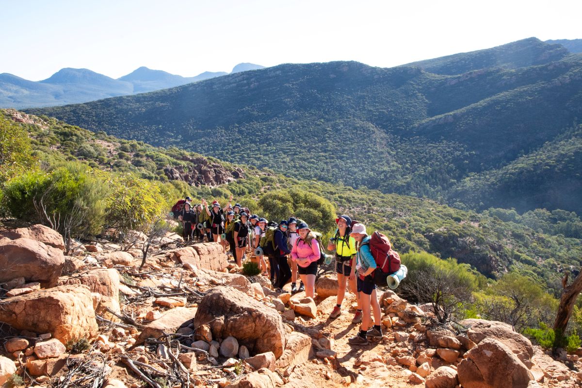 A group of hikers ascending a rocky trail surrounded by greenery and rugged terrain.