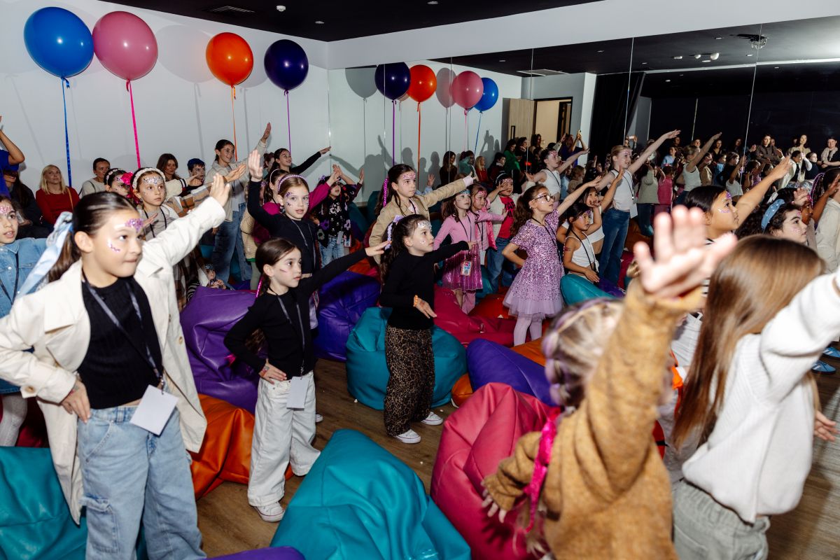 Children playing in a colorful room filled with balloons and various toys scattered around.