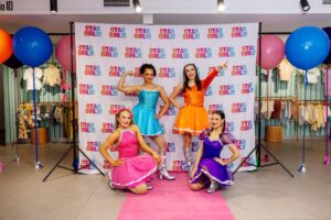 Four girls in vibrant dresses smiling and posing together for a cheerful photo.