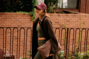 A woman wearing a hat and leggings walks down a city street, surrounded by buildings and greenery.