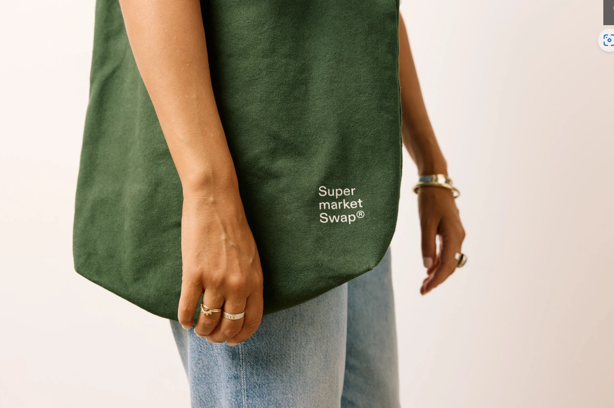 A woman carrying a green tote bag, standing outdoors with a casual outfit.