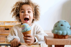 A young girl happily eats an ice cream cone on a sunny day.
