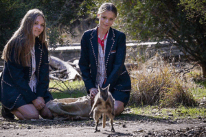 Two girls in school uniforms sitting on the ground, engaged in conversation and enjoying each other's company.