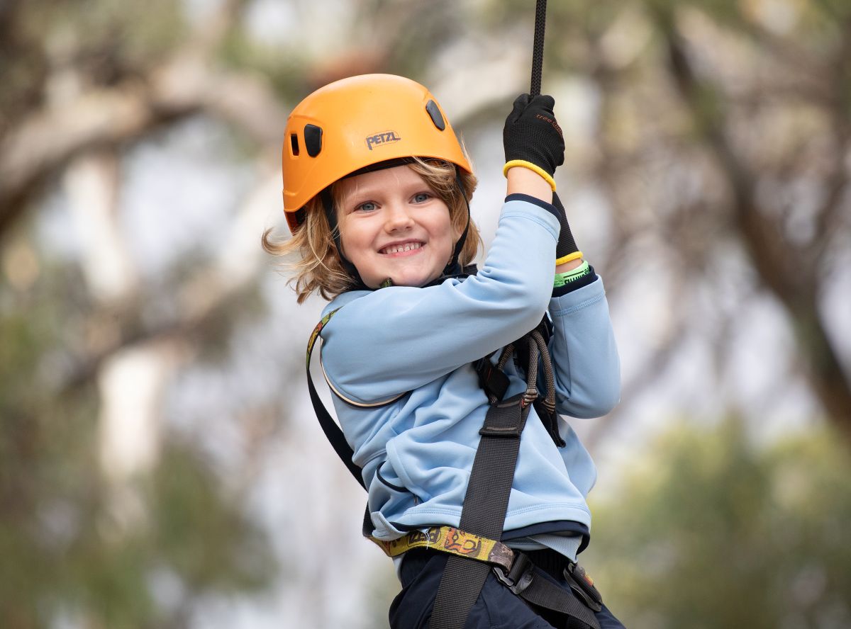 A young child in a helmet grips a rope, ready for an adventure or activity.