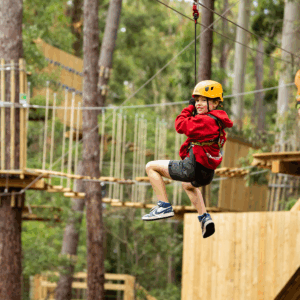 A young boy joyfully glides on a zip line through a lush green forest.