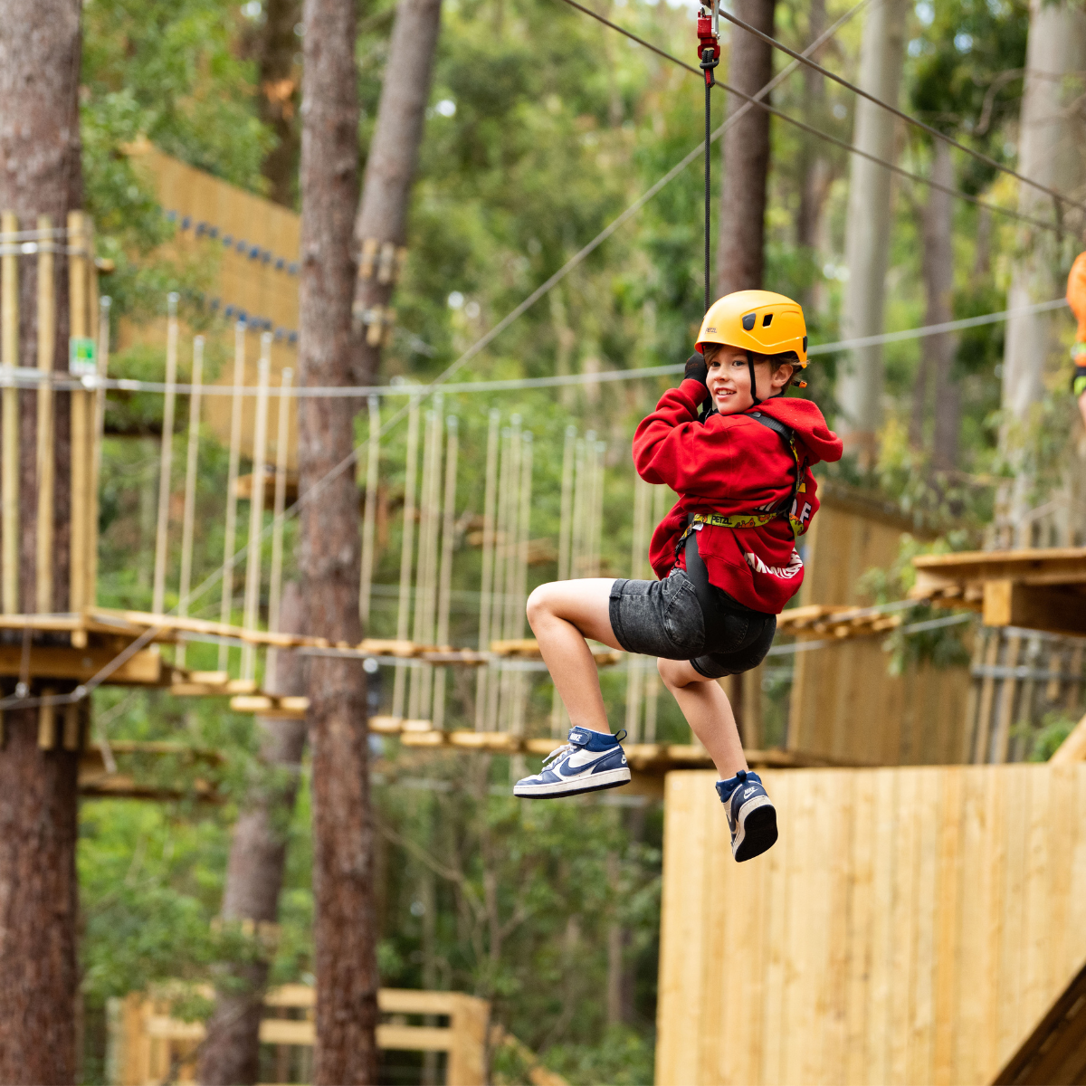 A young boy joyfully glides on a zip line through a lush green forest.