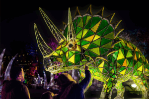 A large triceratops sculpture illuminated at night, showcasing its detailed features against a dark sky.