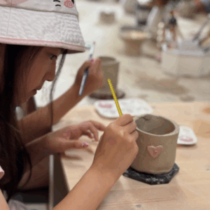 A young girl shapes clay while working on her pottery project at a table.