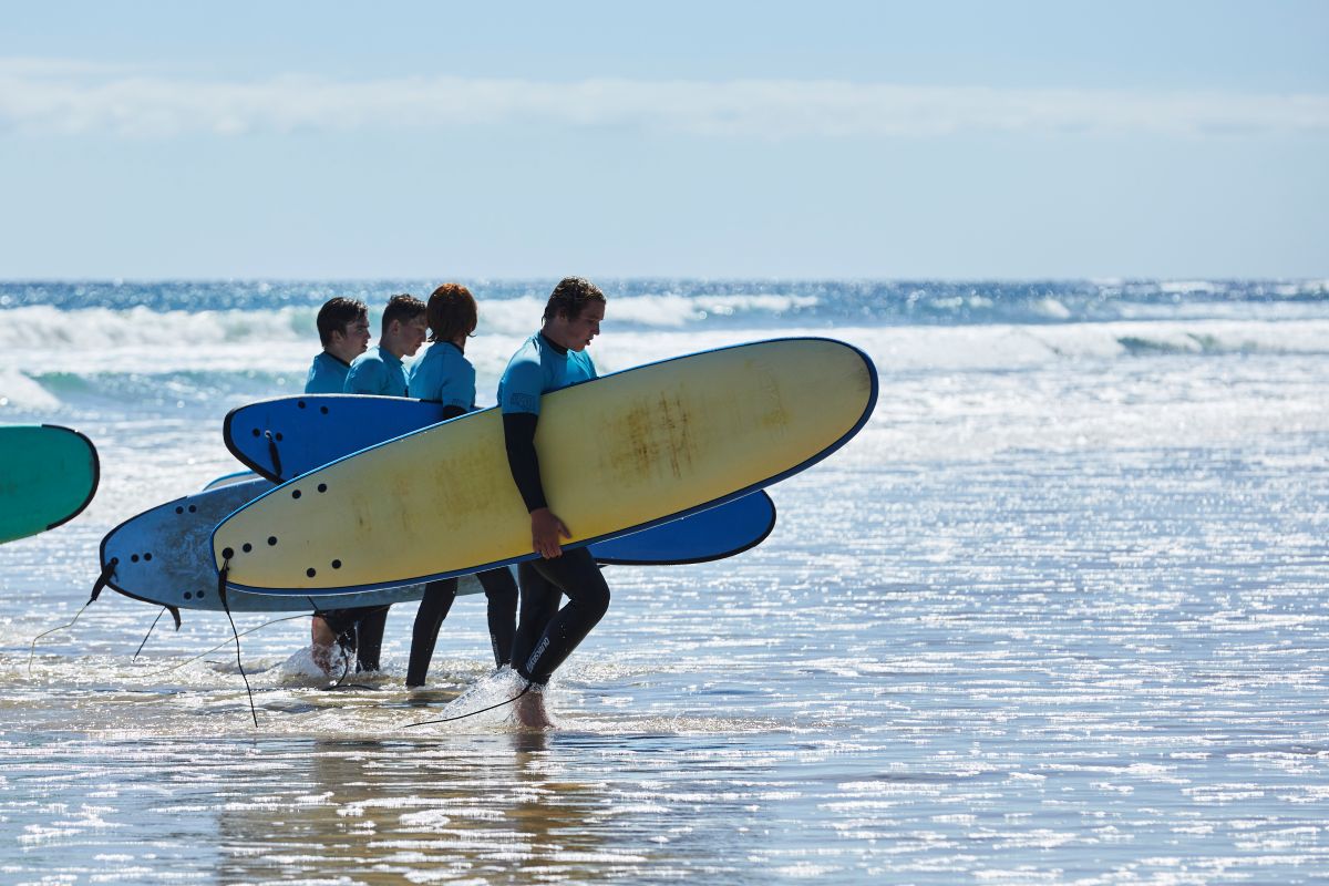 A group of people walking along the beach, each carrying a surfboard under their arms.