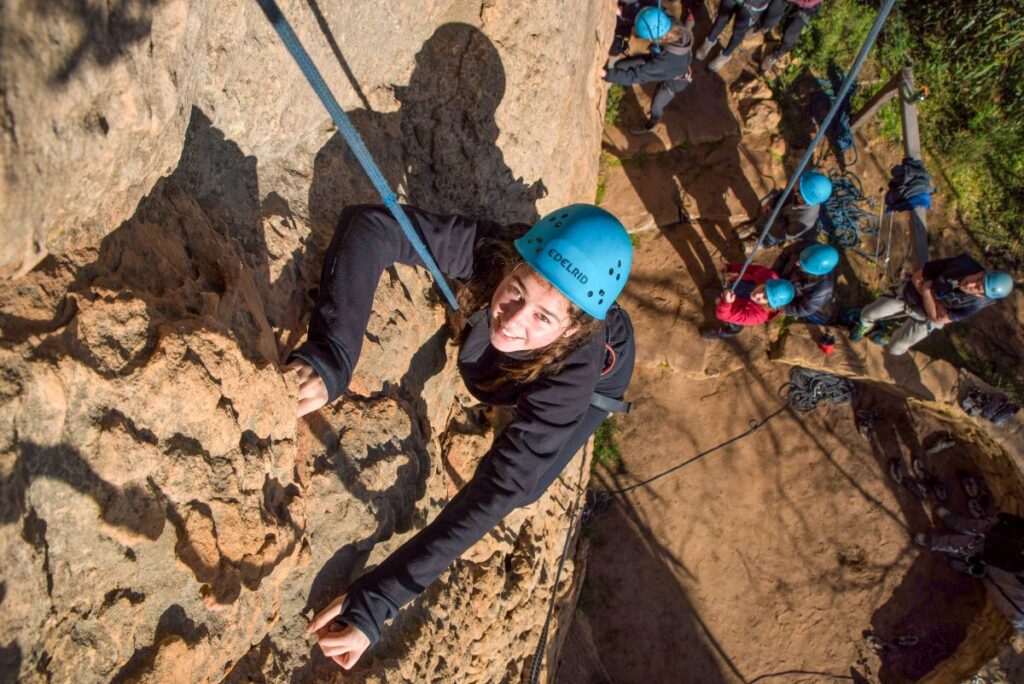 A girl climbs a rock wall, focused and determined, with her hands gripping the holds and her feet positioned carefully.