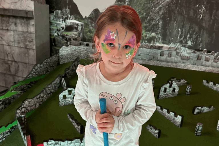 A young girl with colorful face paint smiles while holding a toy in her hand, showcasing her playful spirit.