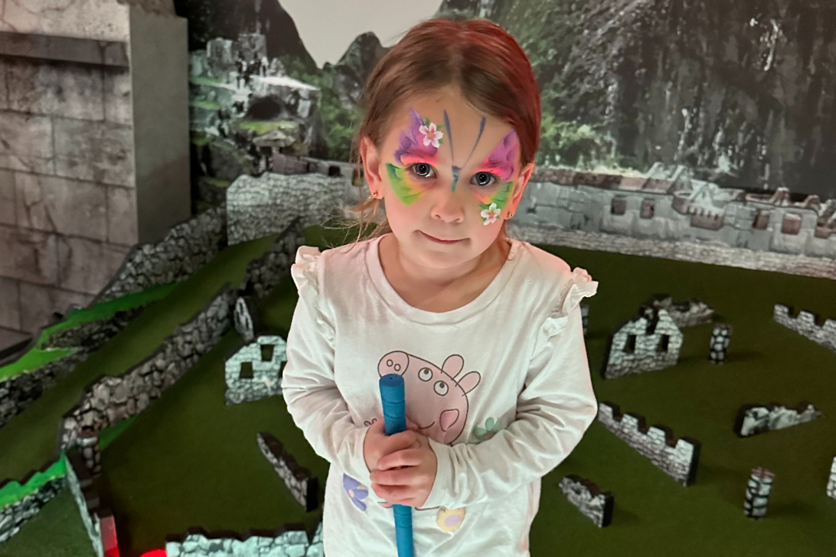 A young girl with colorful face paint smiles while holding a toy in her hand, showcasing her playful spirit.