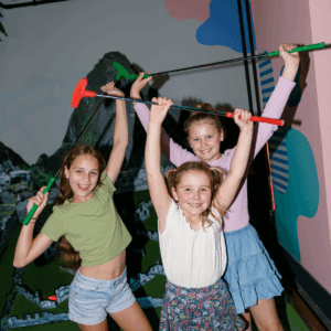 Three girls smiling and holding up golf clubs.