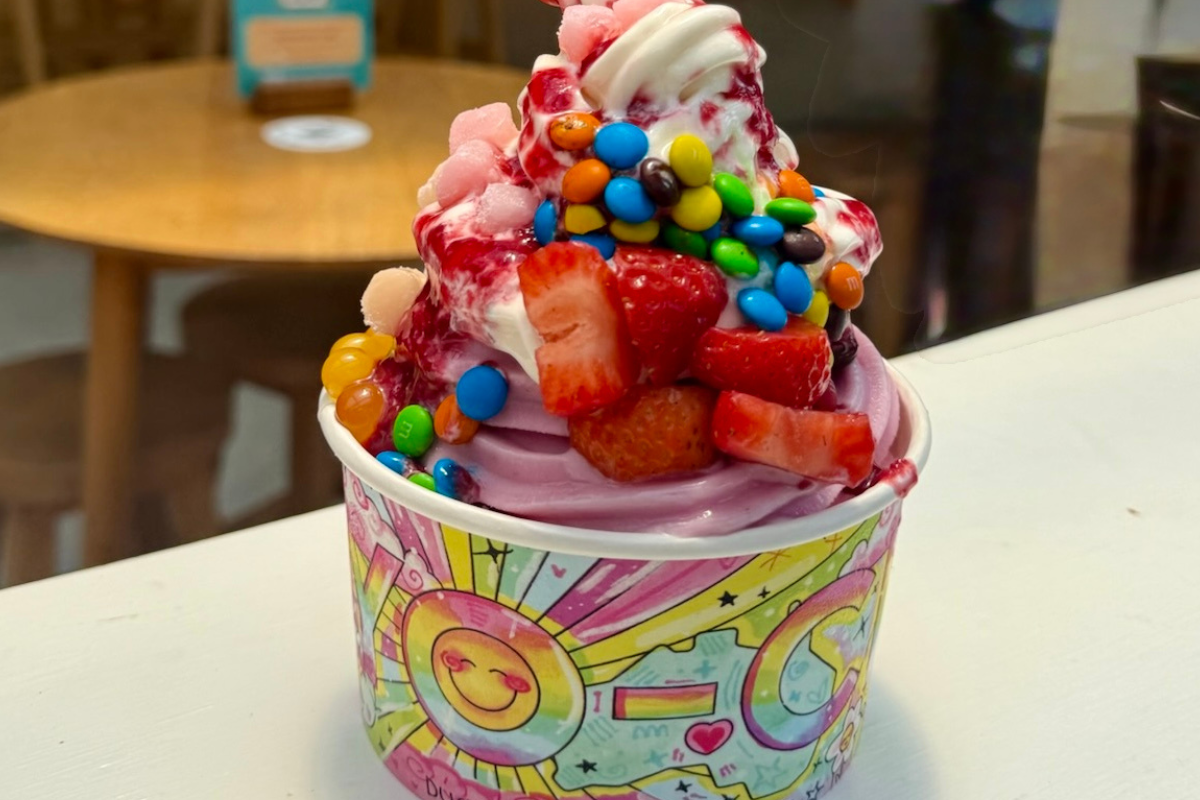A cup of frozen yoghurt topped with vibrant, colorful sprinkles and a cherry on top, set against a neutral background.