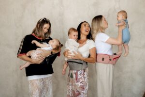 Three women hold babies, while one additional woman cradles a baby, showcasing a moment of maternal bonding.